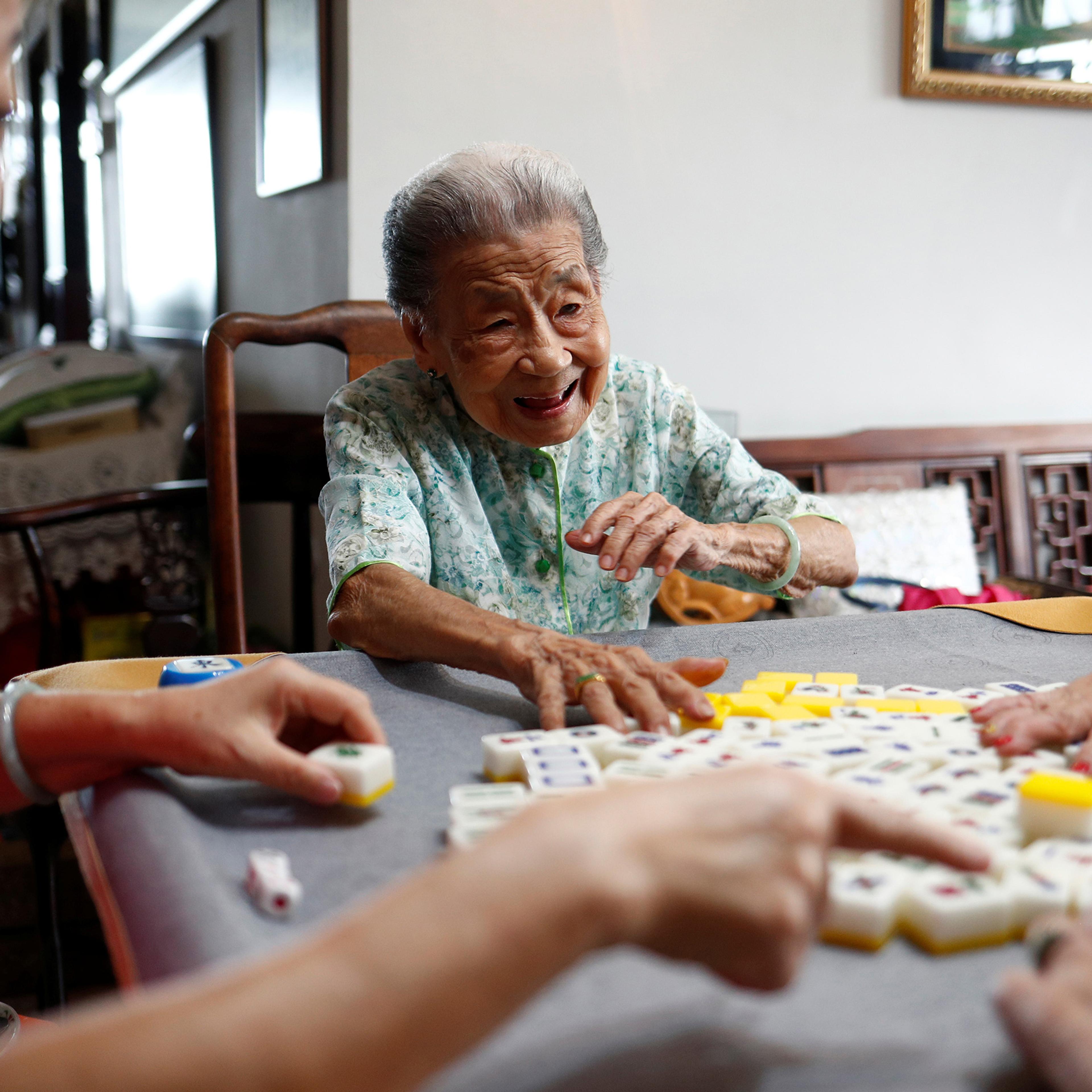 Photo of elderly women playing Mahjong at a table, laughing and engaged in the game in a cosy indoor setting.