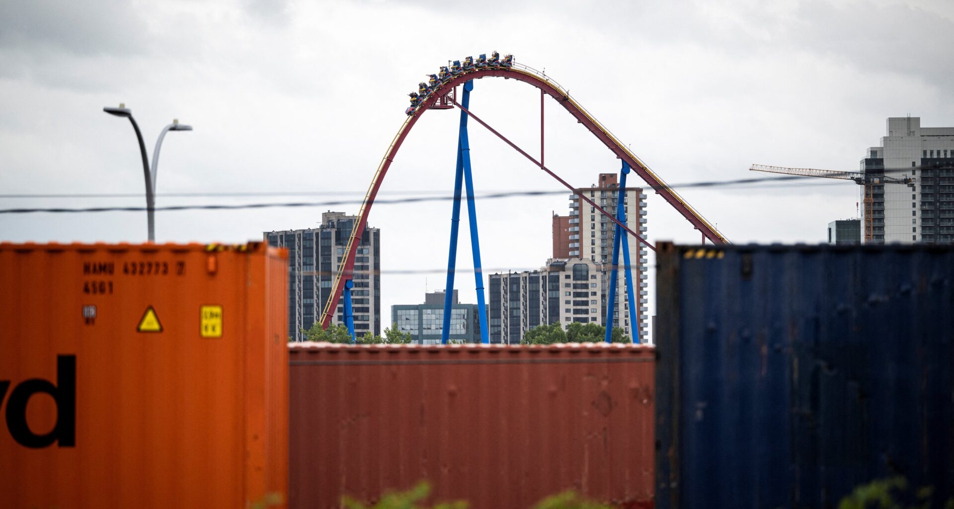 A rollercoaster goes down a hill as shipping containers are seen in the foreground in the Port of Montreal.