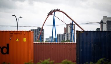 A rollercoaster goes down a hill as shipping containers are seen in the foreground in the Port of Montreal.