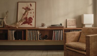 A living room with a textured accent armchair, a floating display of vinyl, a record player, a white table lamp, a leaning painting, and ceramics