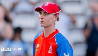 Freya Kemp looking ahead, looking thoughtful, wearing England blue and red One-Day kit, and sunglasses on the back of her cap