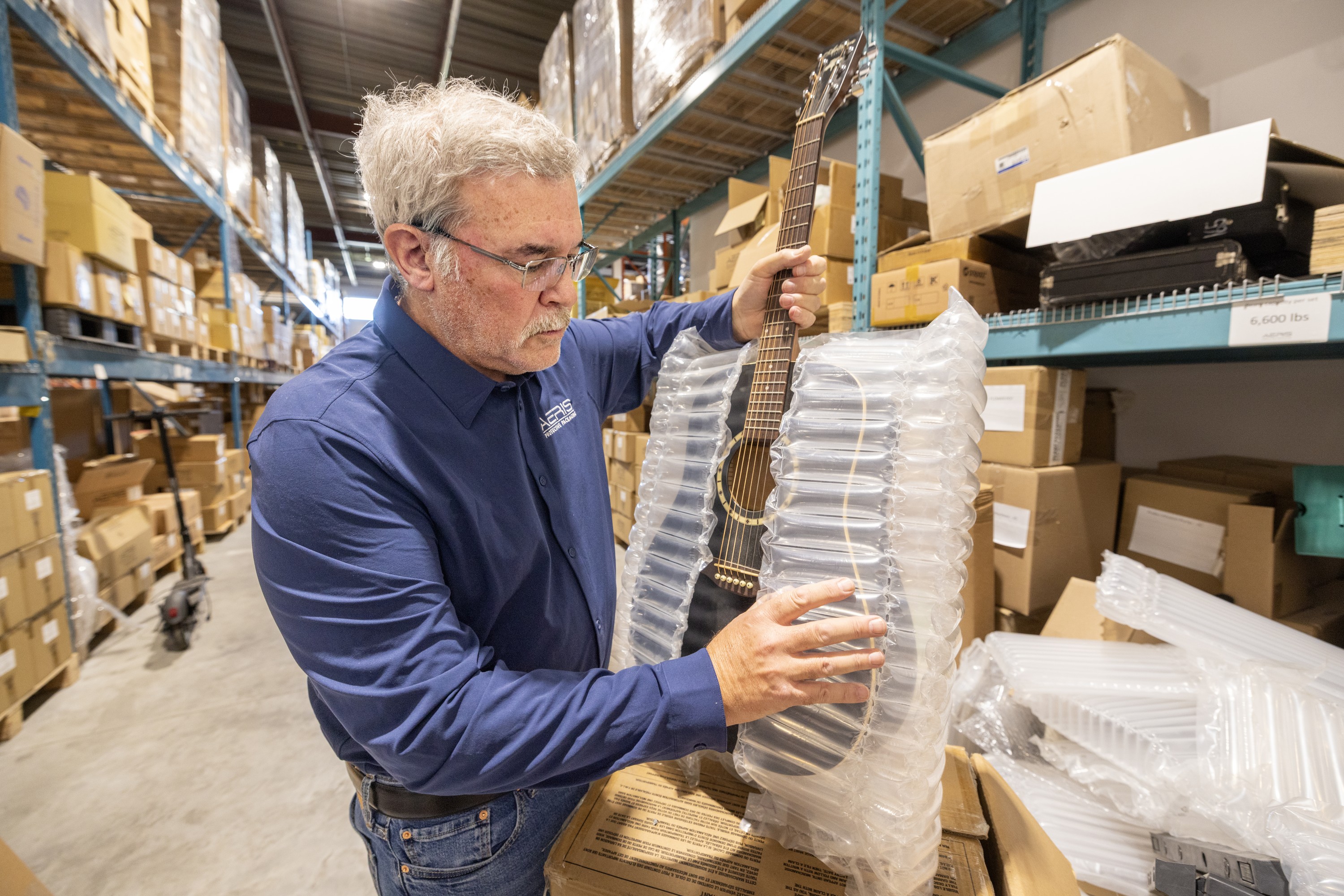 A man wraps a guitar in protective packaging in a warehouse