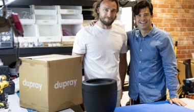 Two guys standing beside a box with their company name on it and a small, portable humidifier on a table in front of them.