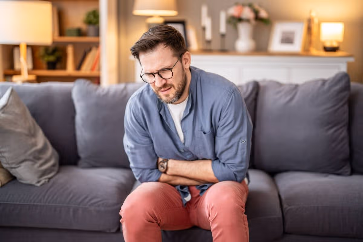 Man suffering from severe abdominal pain and indigestion while sitting on a couch