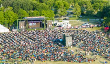 Crowd of people in an outdoor setting within trees and near a stage.