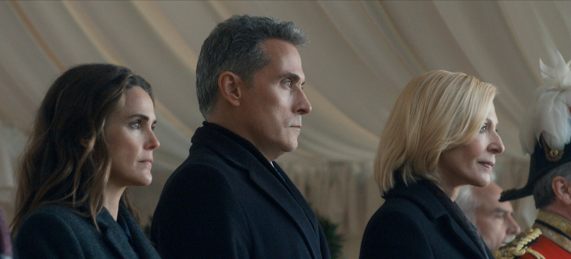 Two women flank a man in a dark coat.