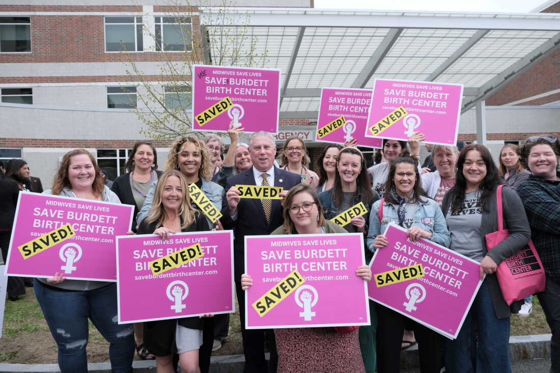 State Assembly member John T. McDonald III holds a sign that says "SAVED!" He's standing in the middle of a group holding signs that also say "SAVED!" and "Save Burdett Birth Center." 