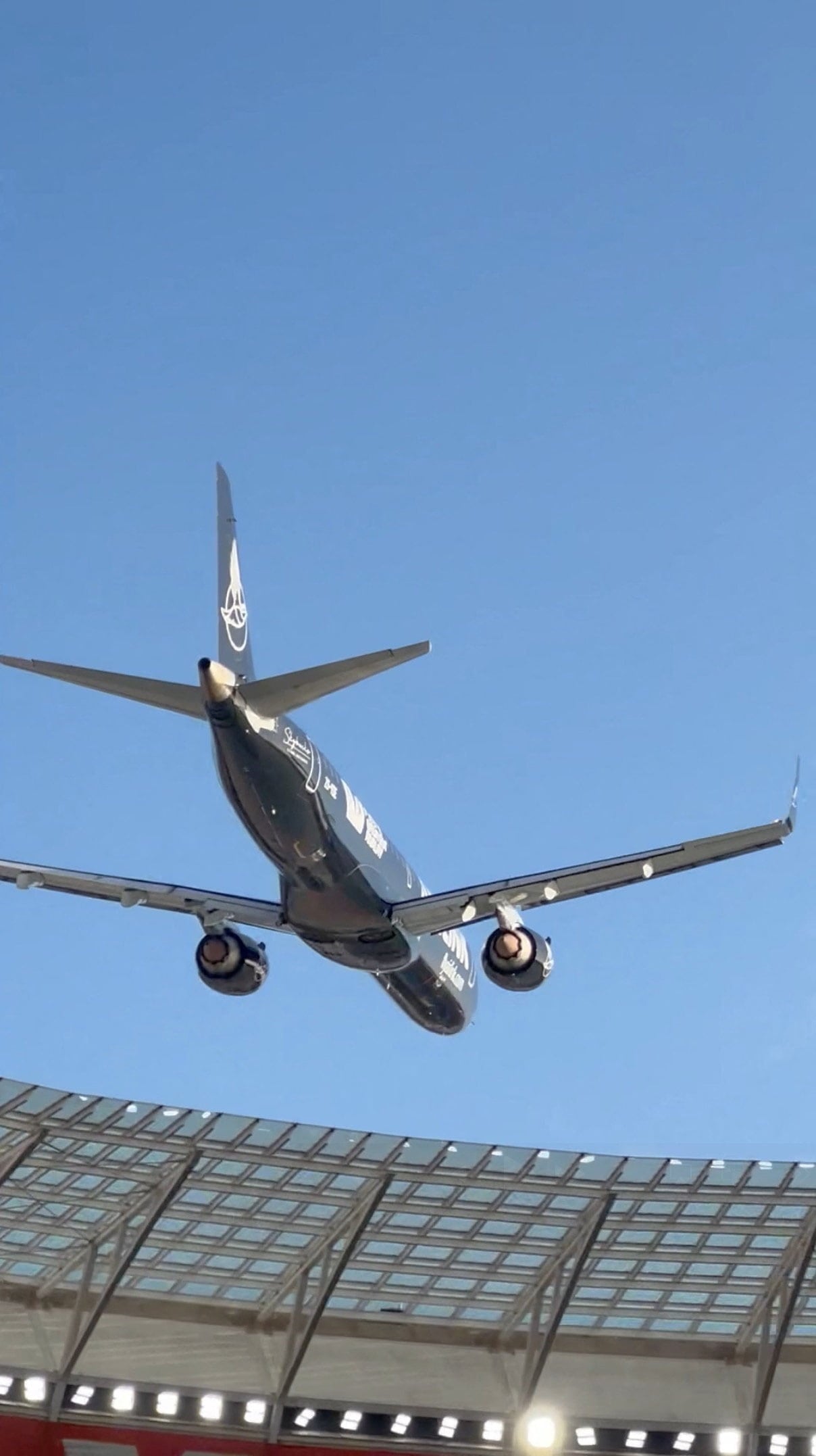 A dark-coloured, widebodied aircraft visible above a stadium, shot from below.
