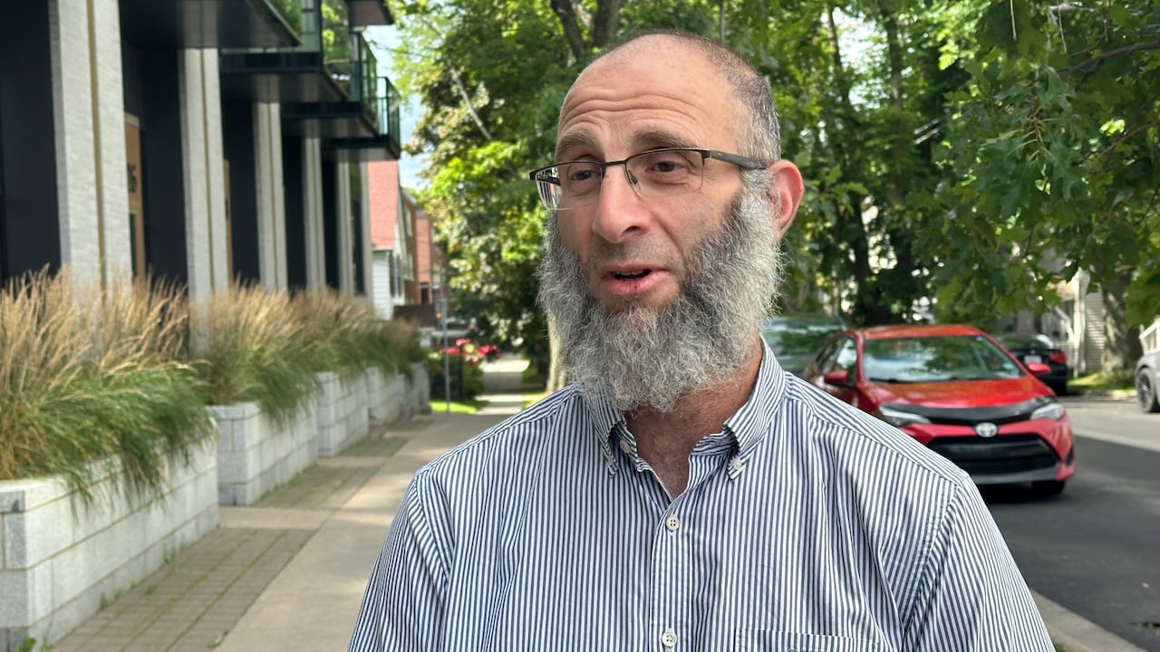A man in glasses with a beard on a sidewalk.