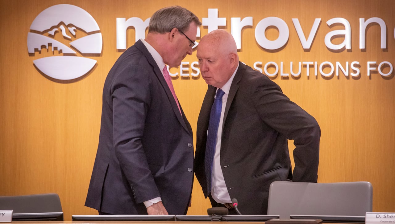 Two white men speak to each other in front of text that reads 'Metro Vancouver'.