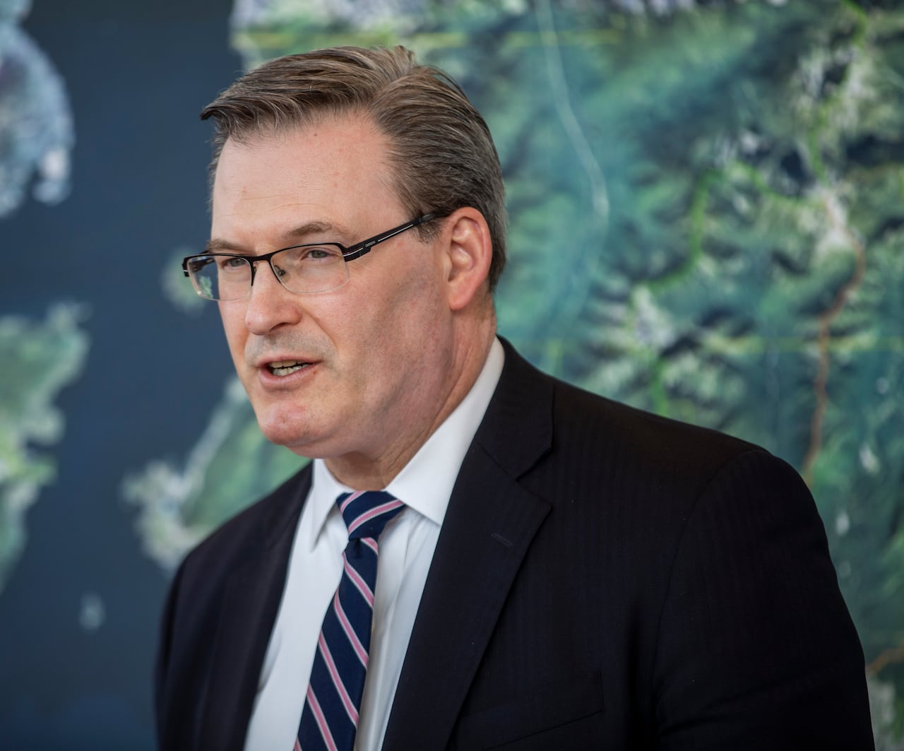 A white man is seen in front of a map.