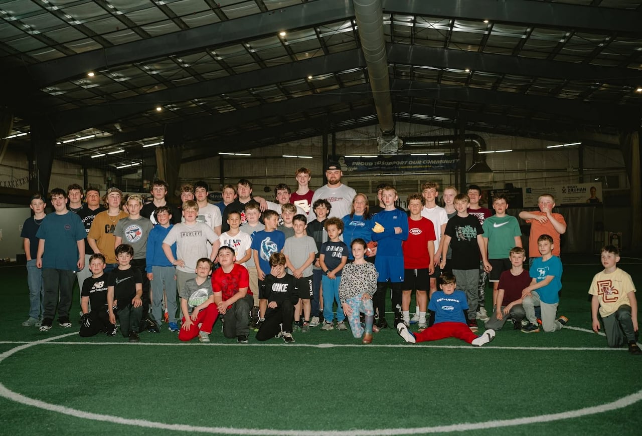 A few-dozen youth are shown at an indoor turf facility, along with a professional football player who towers over them.
