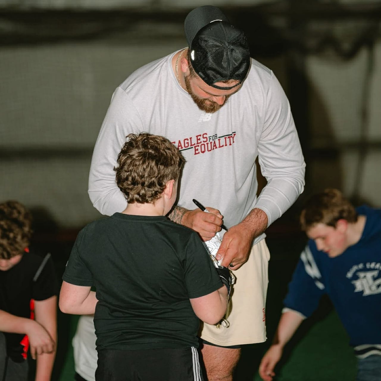 A hulking football player signs an autograph, towering over the fan.