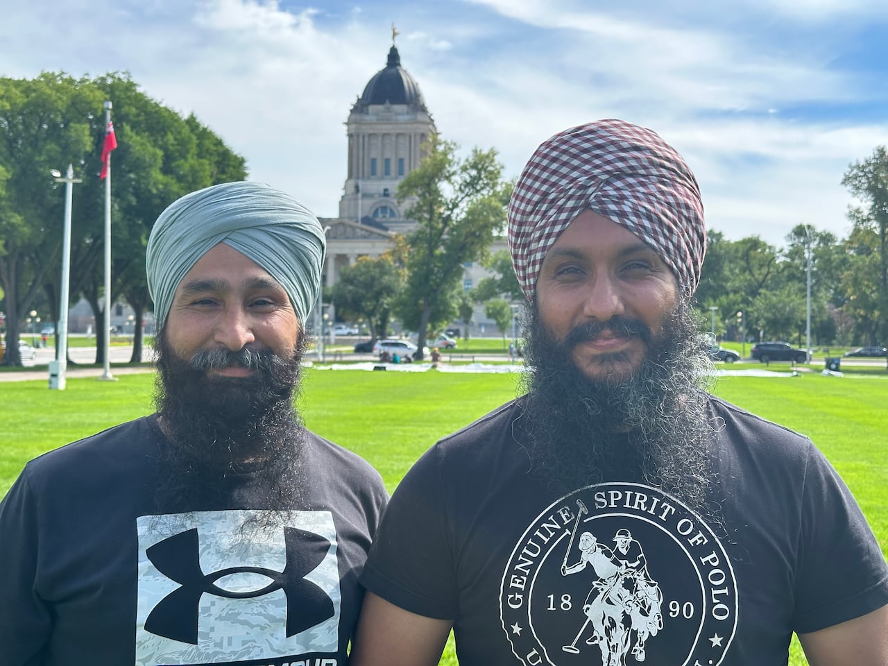 Two man standing in Memorial Park with the Manitoba legislature in the backrgound.