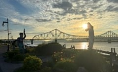 The sun sets over a bridge and river.