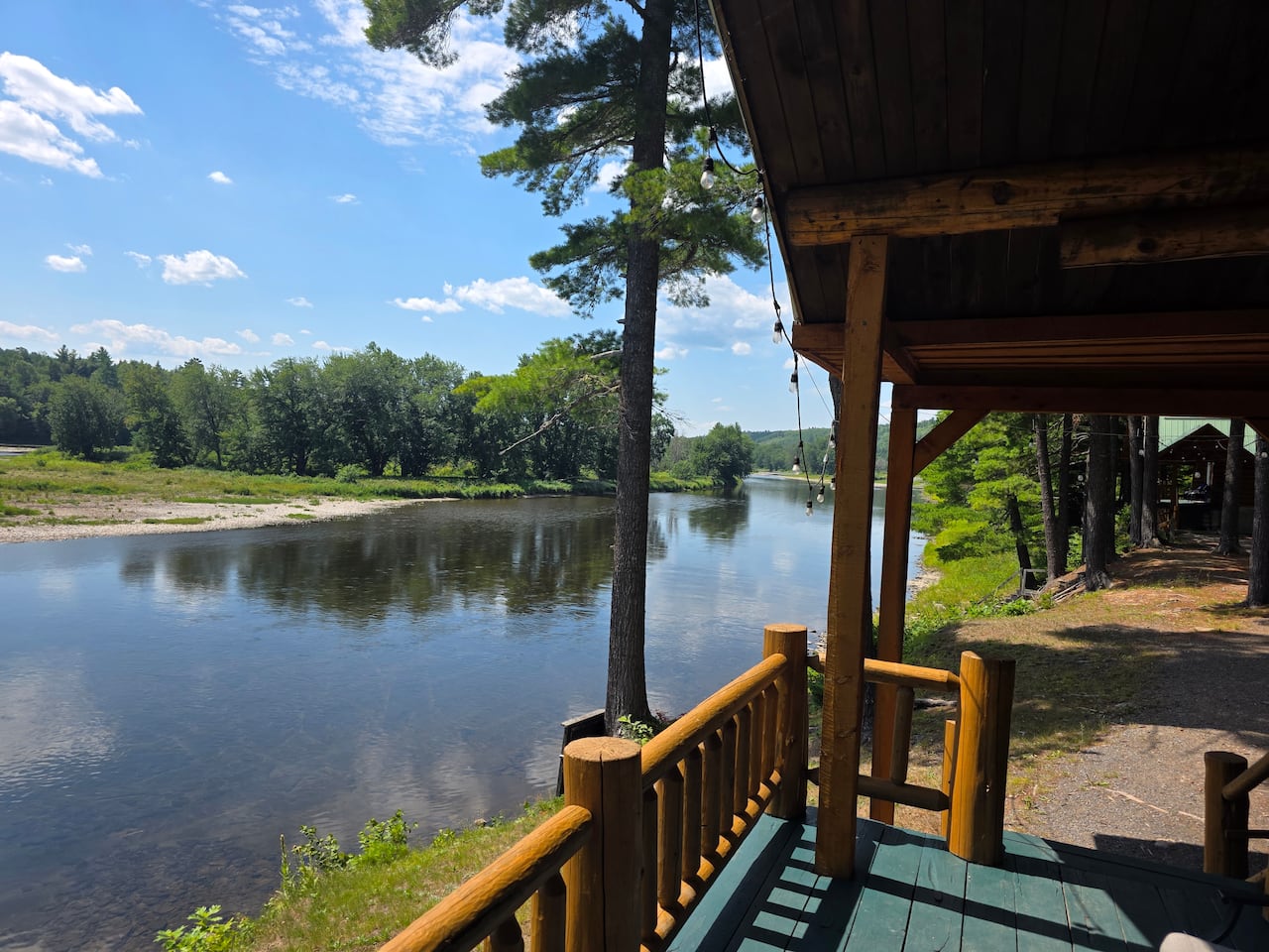 A cabin porch overlooks a river on a sunny day.
