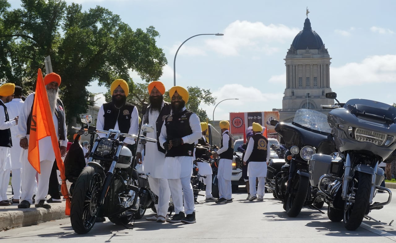 A small group of motorcyclists posing for a photo with the Manitoba Legislature building in the background.