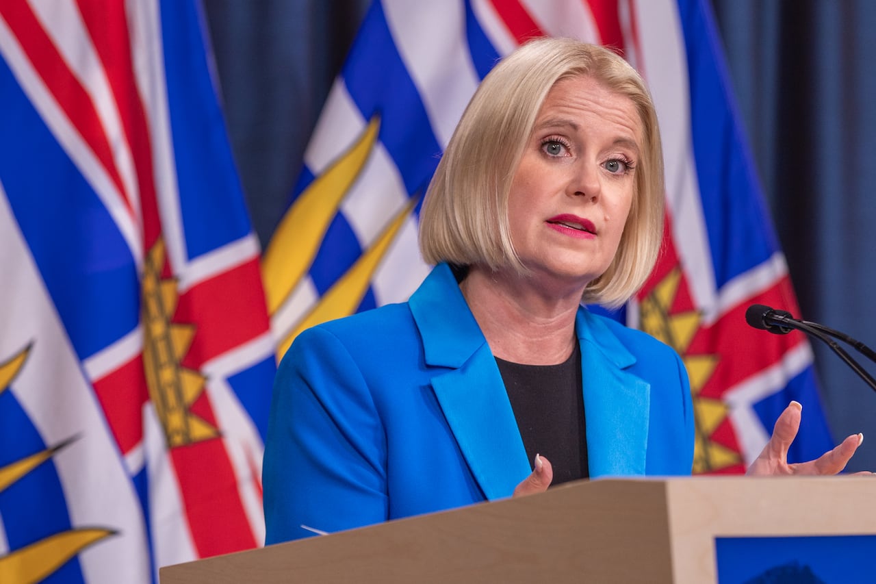 A blond woman in a blue coat speaks at a podium 