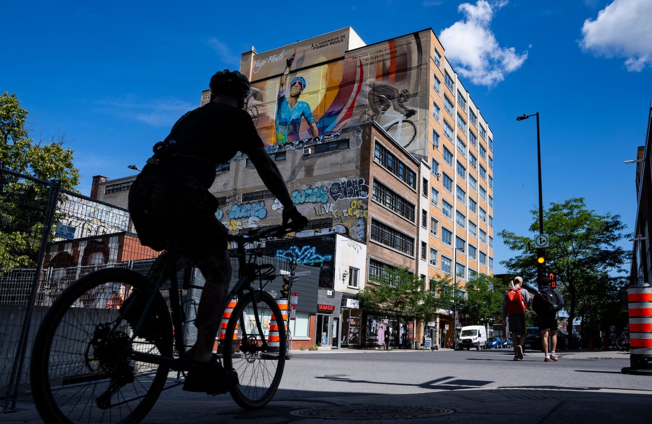 The shadow of a cyclist rides past a colourful mural of a cyclist riding his bike and raising his finger to the sky in celebration.