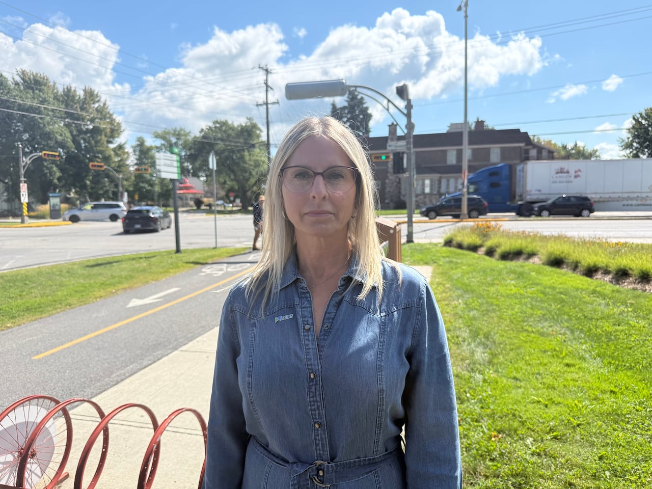 women with blonde hairs and blue jean dress stands in front of high way 20
