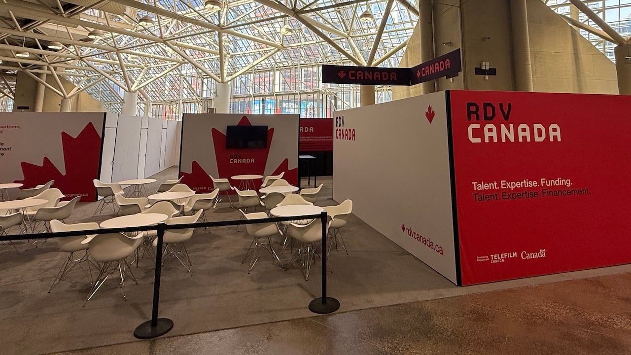 Inside a convention centre, several chairs and tables are set up next to a sign for the Canada Pavillion at TIFF Market.