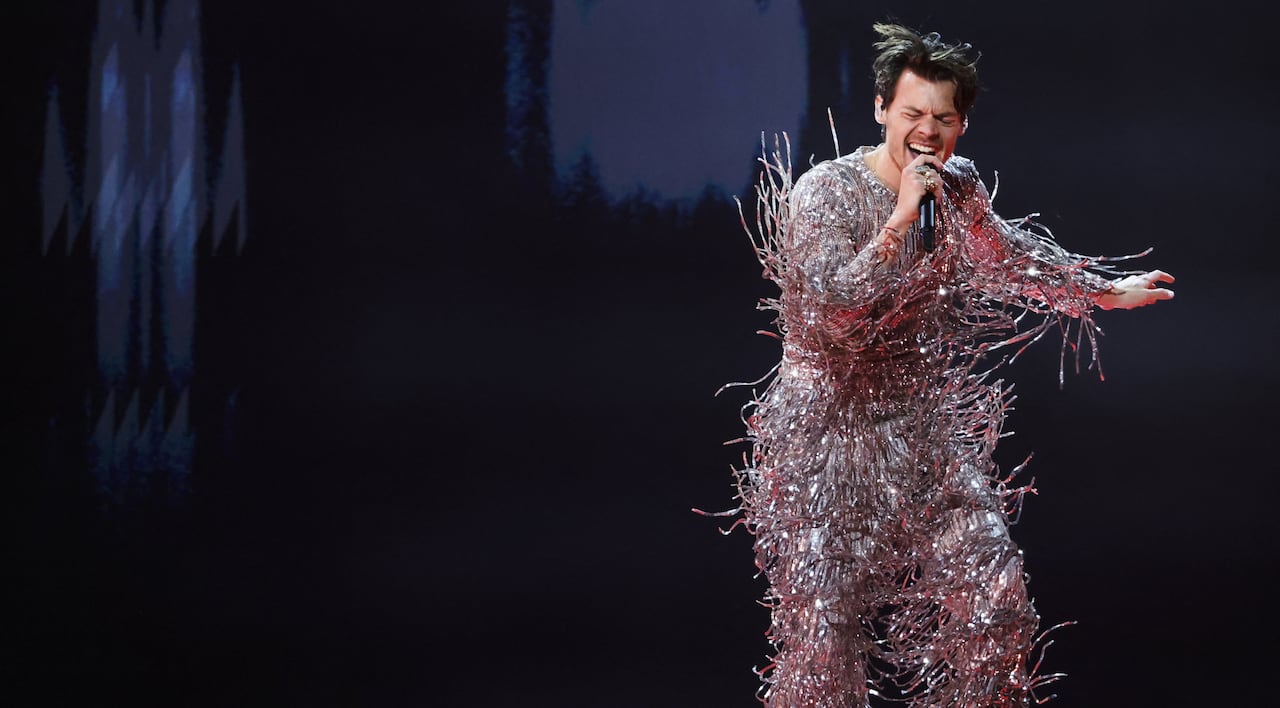 A man sings energetically in a full fringe silver jumpsuit.