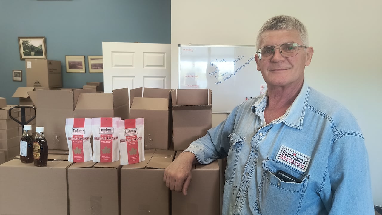 A man with glasses next to a stack of boxes and jars of maple syrup