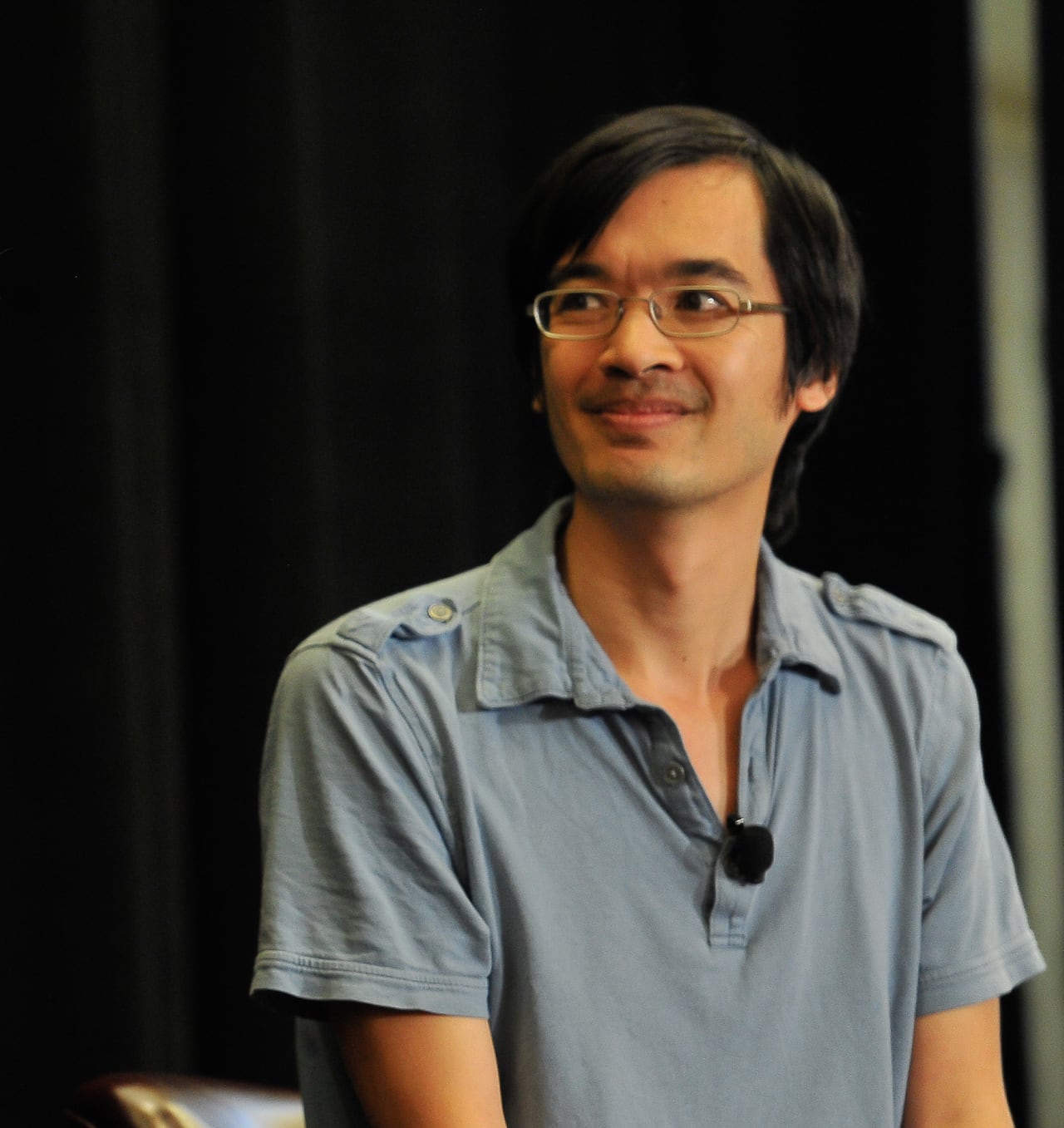 A man in a blue shirt looks to the left on a stage.