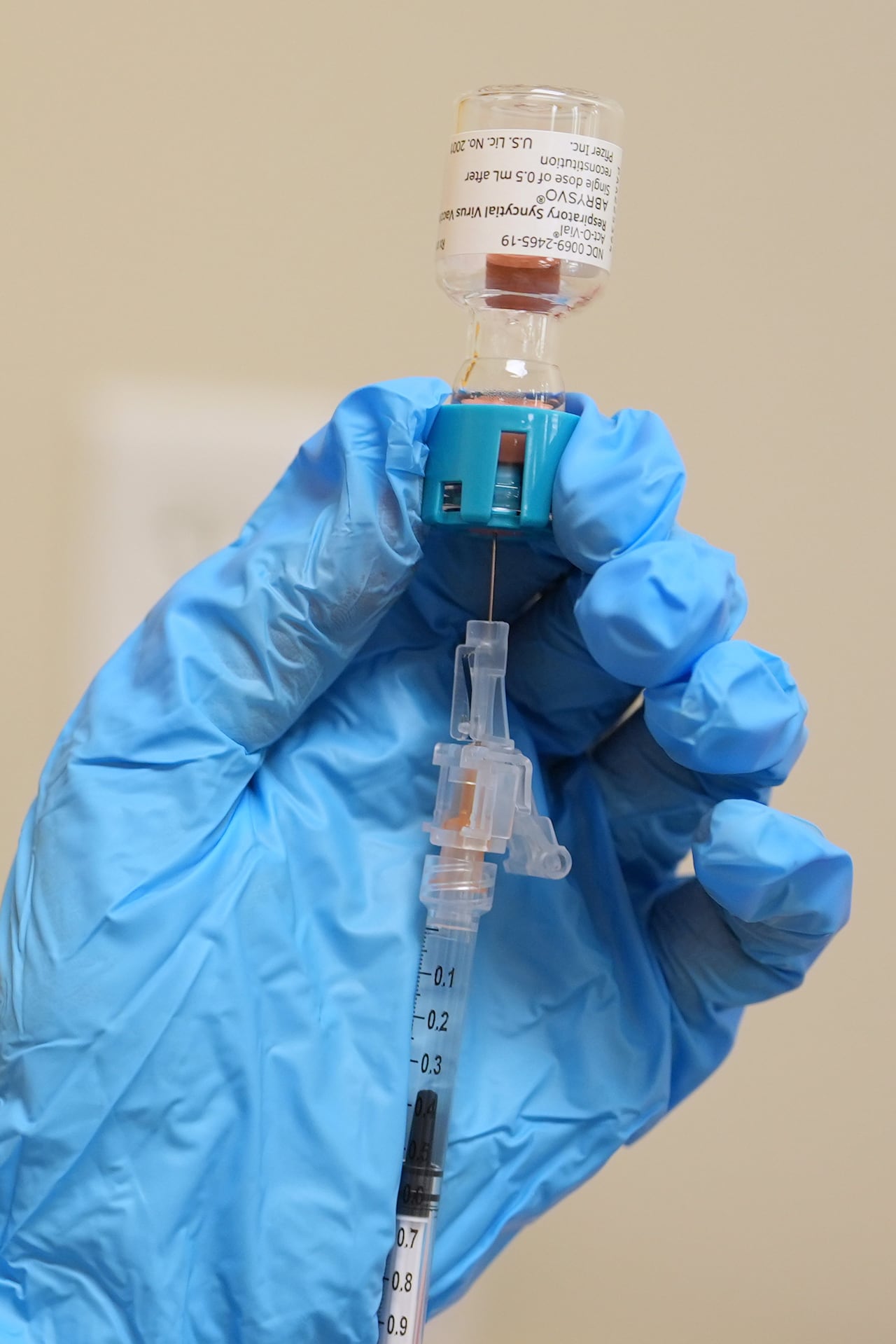 A pharmacist wearing blue gloves draws a dose of respiratory syncytial virus (RSV) vaccine into a syringe.