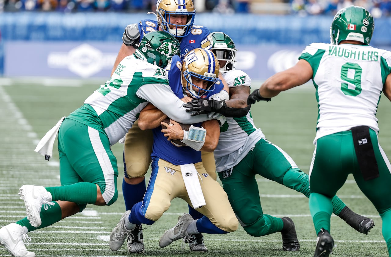 Football players in white and green uniforms tackle a player in a blue and gold uniform