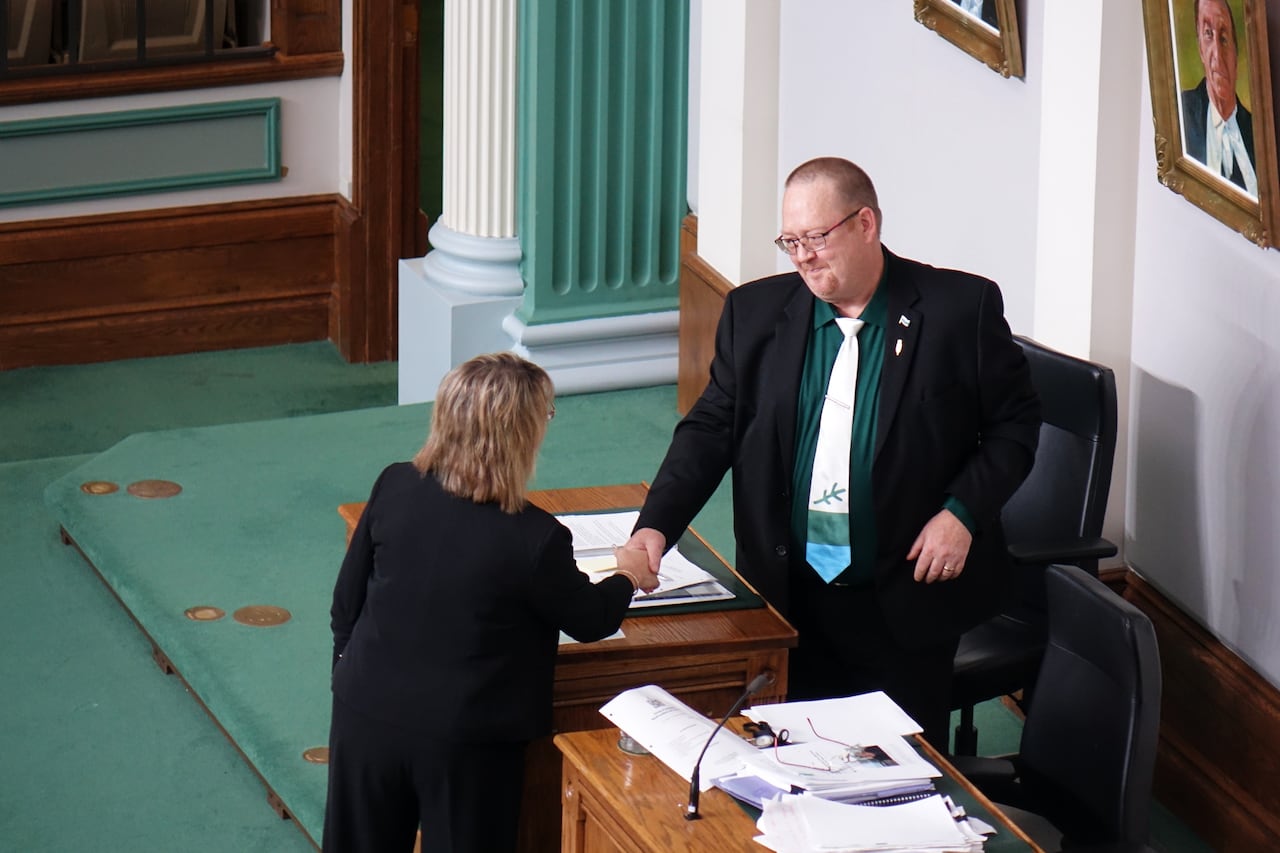 A man and a woman shaking hands on a legislature floor.