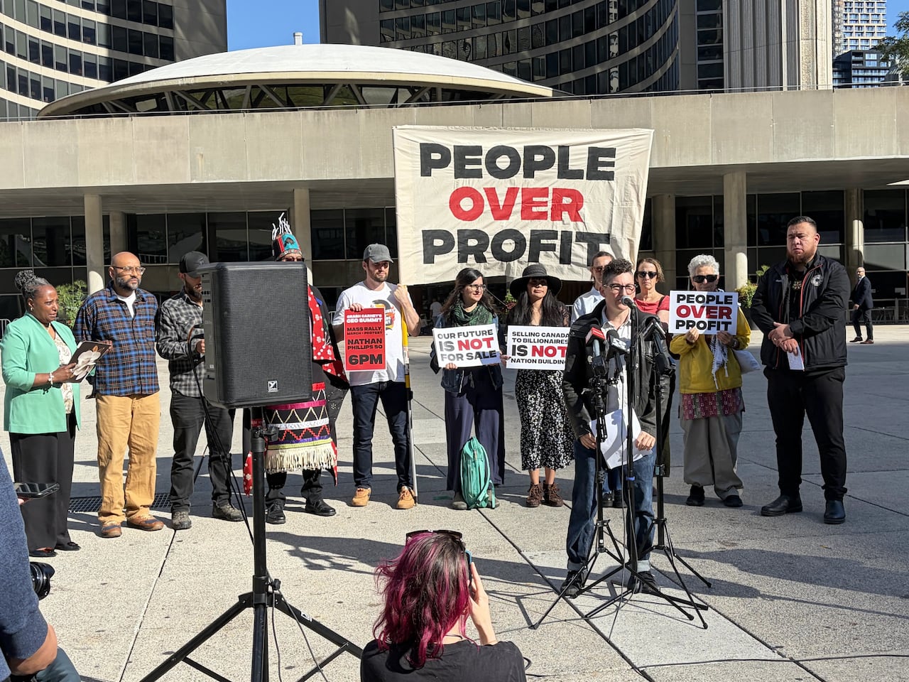 Person stands at microphone in front of city hall at a news conference protesting the Canada Investment Summit.