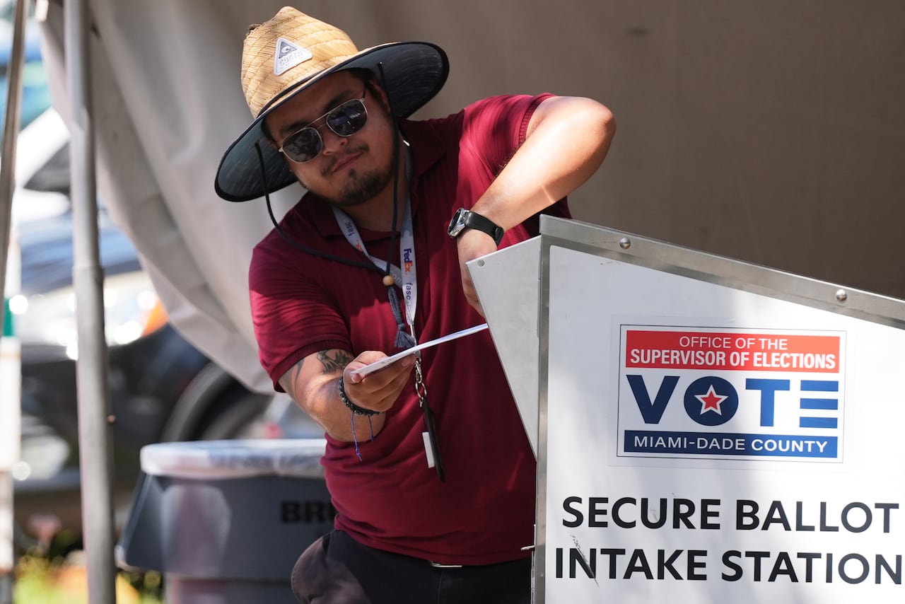 Man in a hat places an envelope in a mailbox that has the words Secure Ballot Intake Station on it