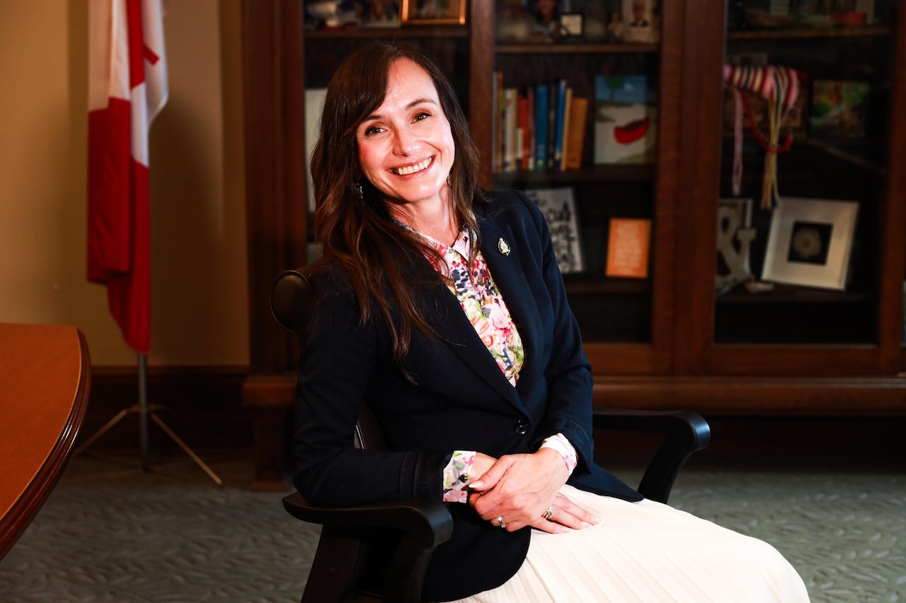 A woman smiles as she sits on a chair.
