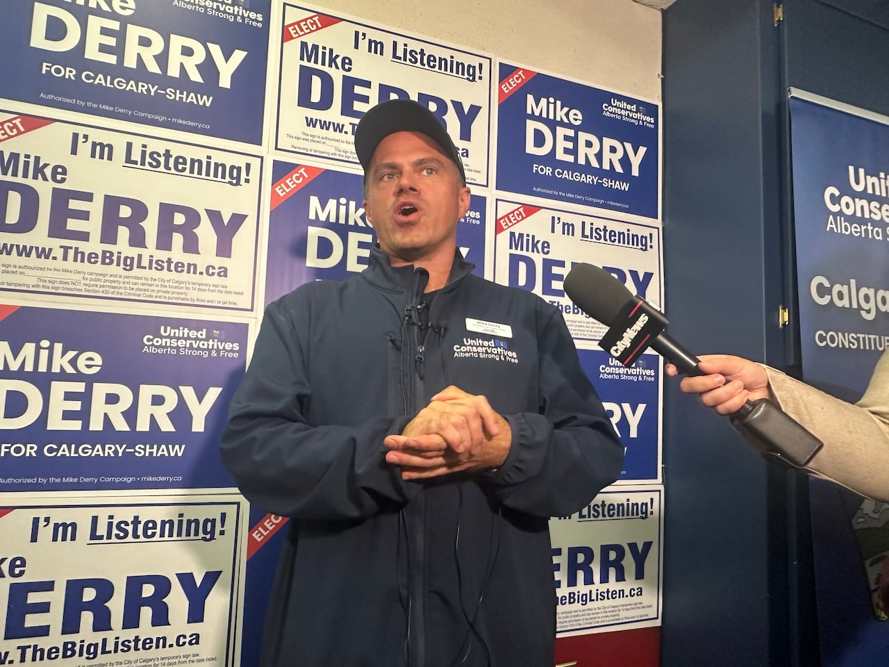 A man wearing a baseball cap speaks to a reporter holding a microphone.