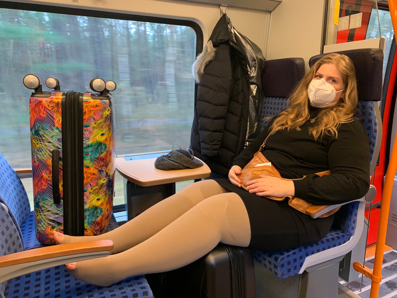 A woman sits on a train with her legs up on the seat across from her. She's wearing compression socks.