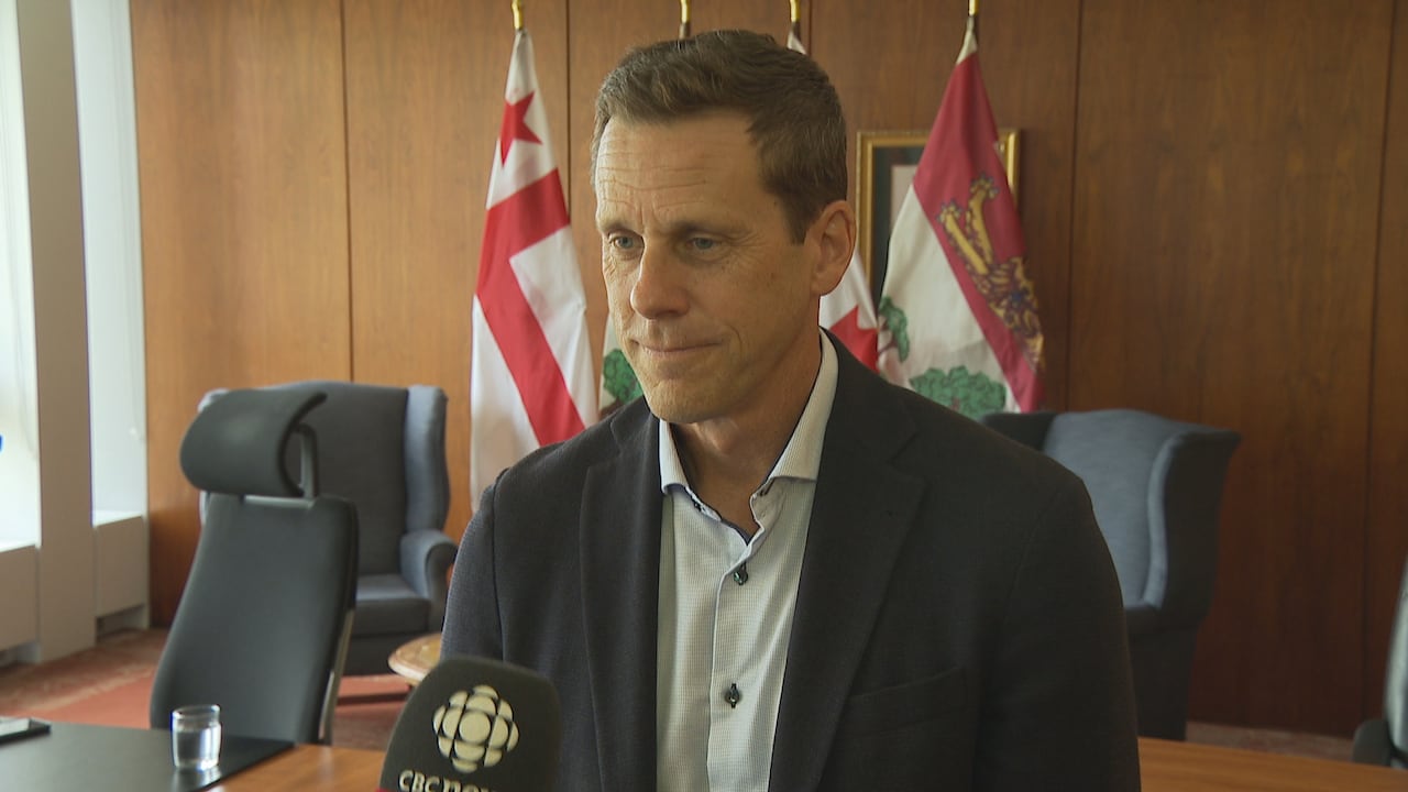 A man in a suit and tie look to the left in a tv interview in his office