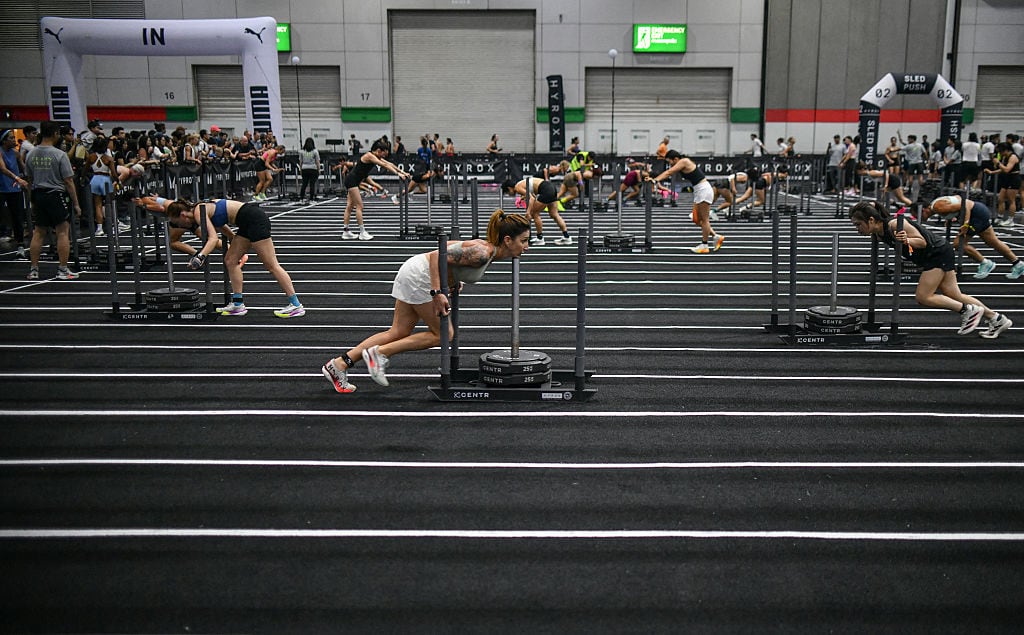 Female athletes push weights across a gym floor.