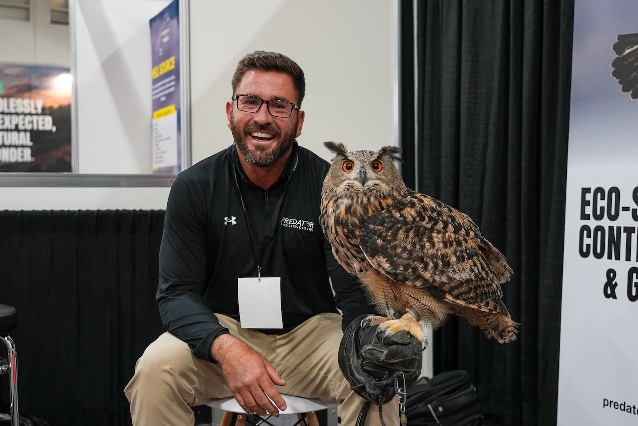 A man smiles while a large owl rests on a gloved hand.