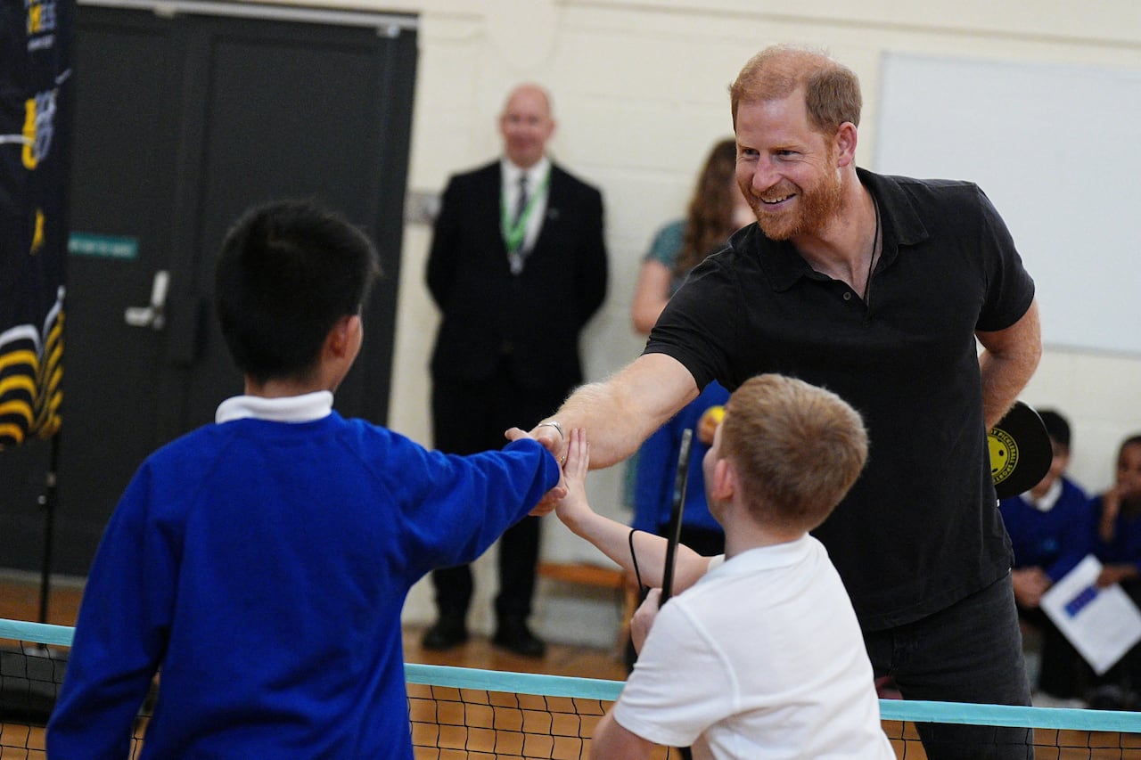 An adult shakes hands with a child over a net in a gym.