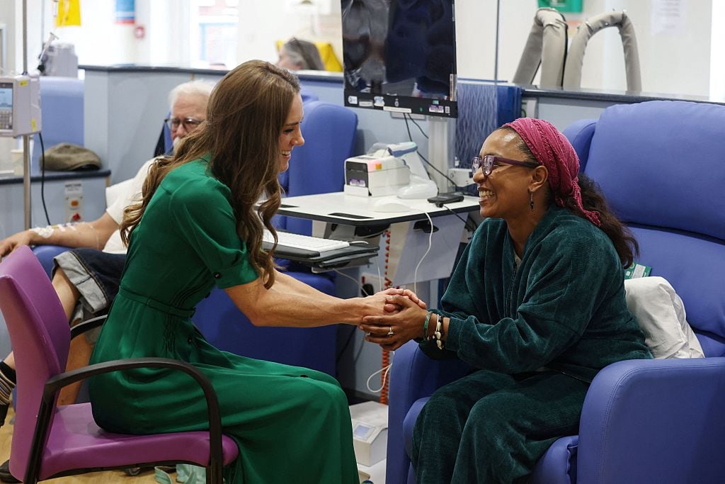 Two people hold hands while sitting in a hospital treatment area.