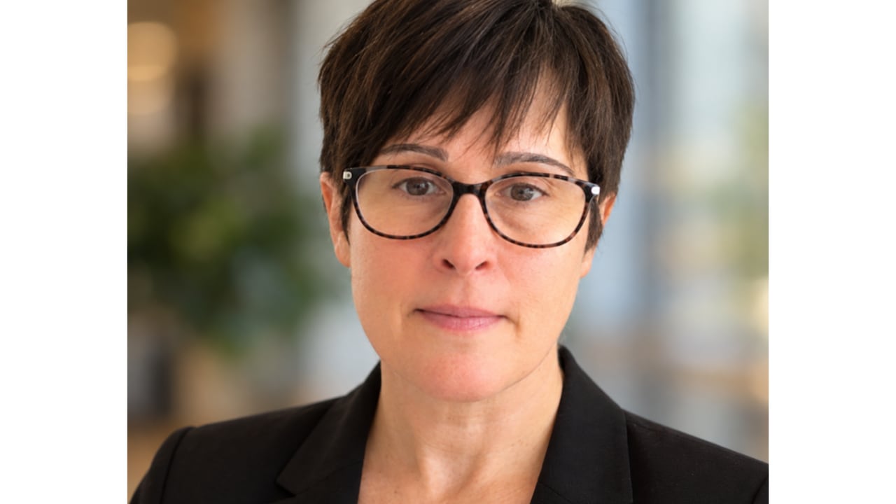 A woman wearing glasses and short dark hair smiles at the camera.