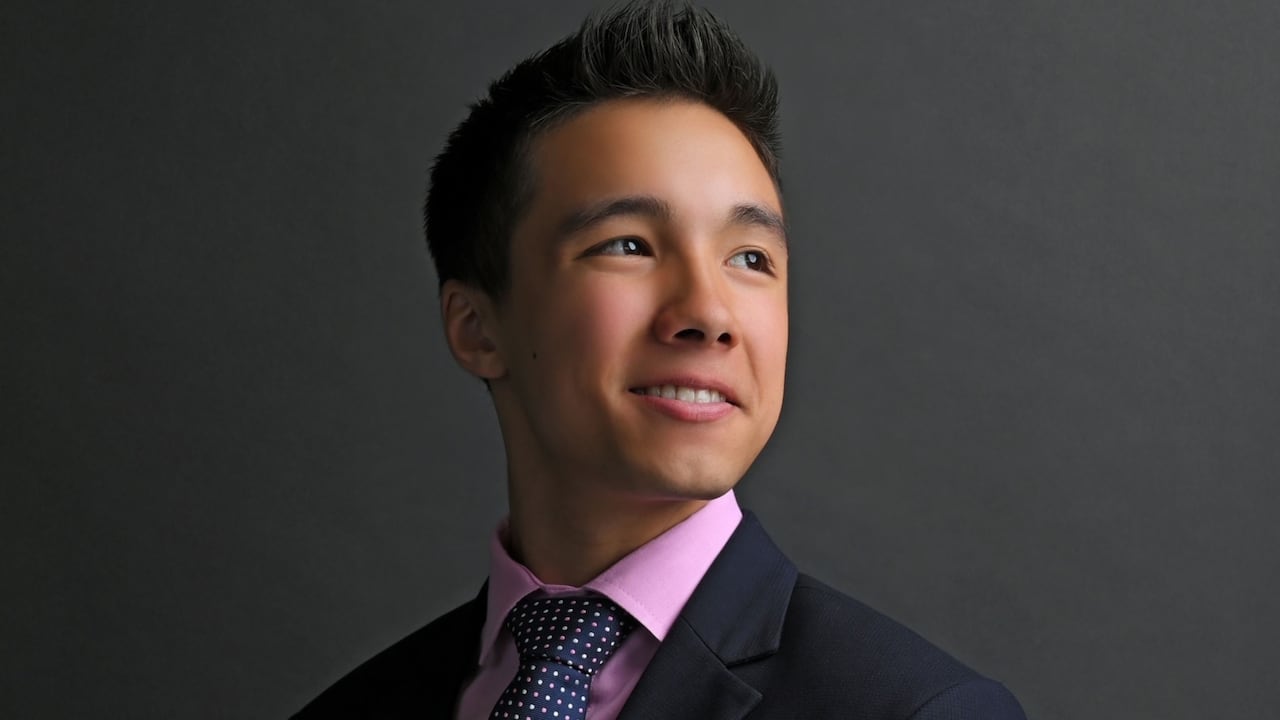 A young man wears a suit and smiles off to the side.
