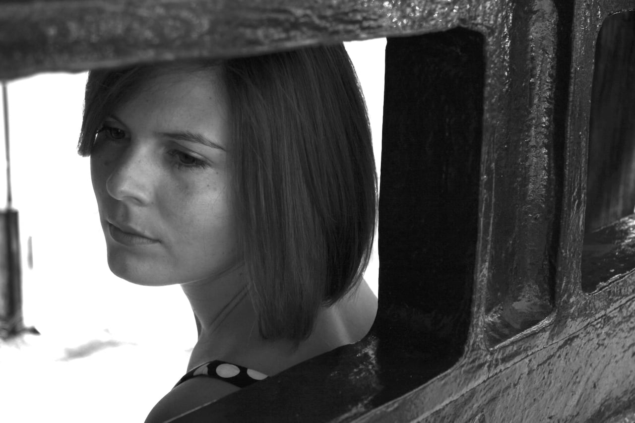 In an artistic black and white photo girl with a bob looks through a window.