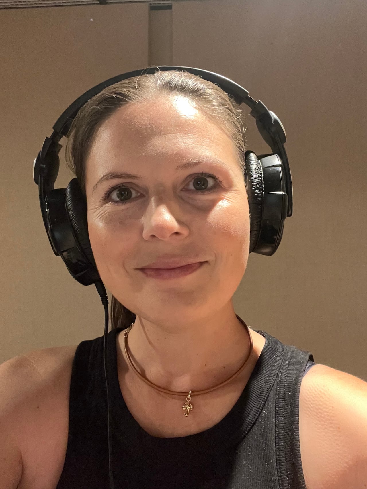 A woman with brain hair slicked back wears headphones and a black tank top.