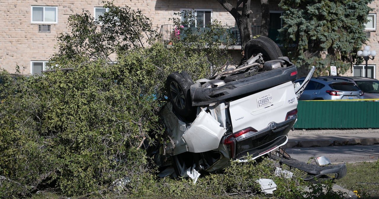 A white vehicle lies upside down on the grass of a median.