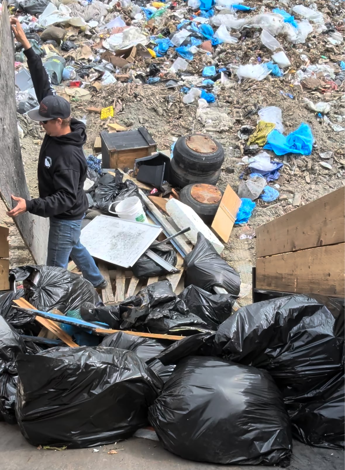 A man pulling garbage out of the back of a dumptruck