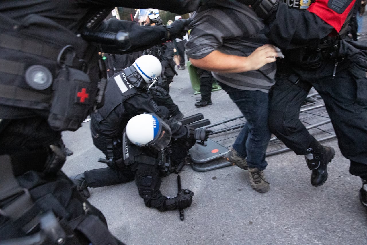 Two police officers on the ground with a metal barrier over them.