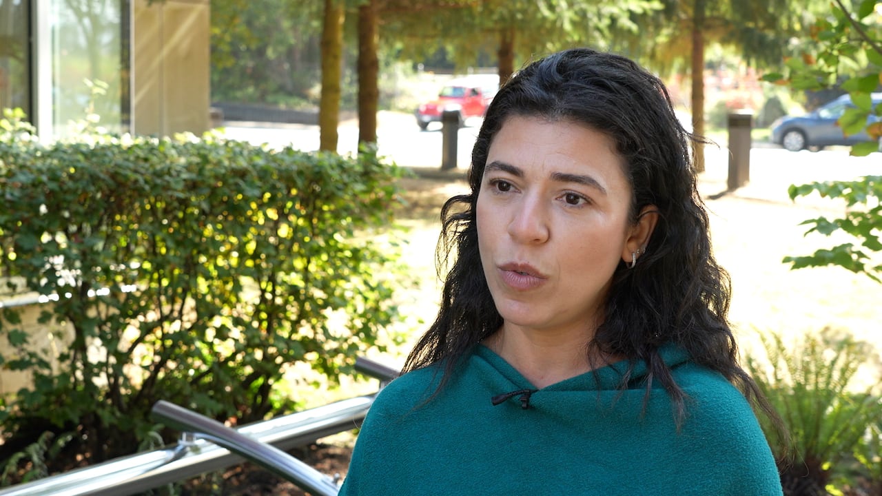A woman in a blue top speaks outdoors.