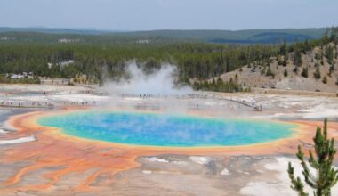 A bright blue pool with steam and ringed in rainbow hues plus people on boardwalks around it.